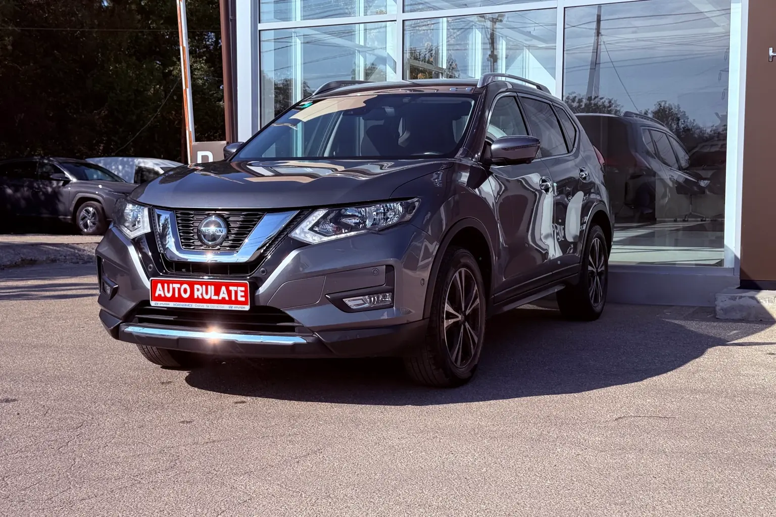 SUV Nissan X-Trail rulat, cu plăcuța „Auto rulate”, parcat în fața unui showroom auto