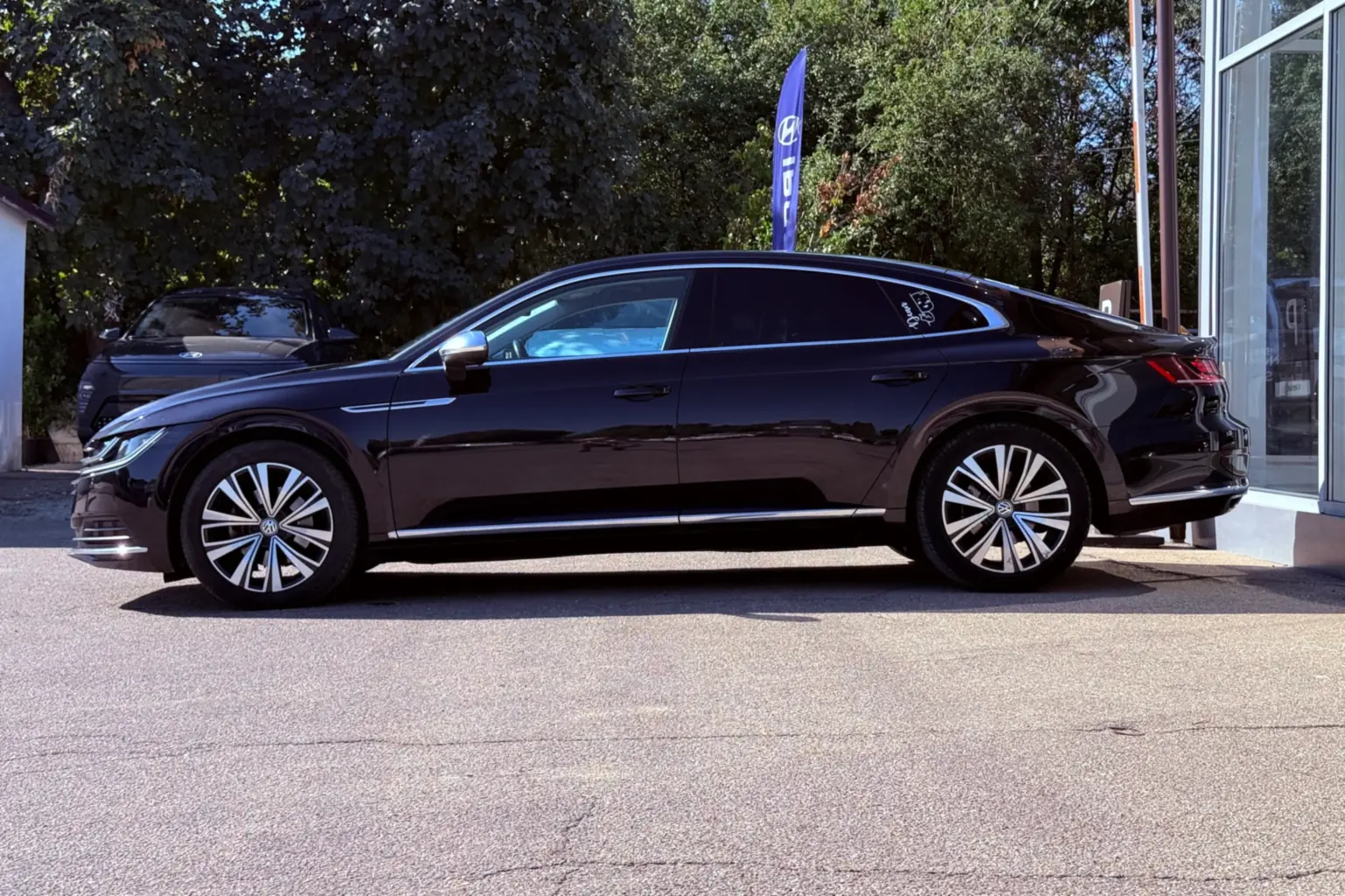 Volkswagen Arteon negru, fotografiat din profil, parcat în fața unui showroom auto